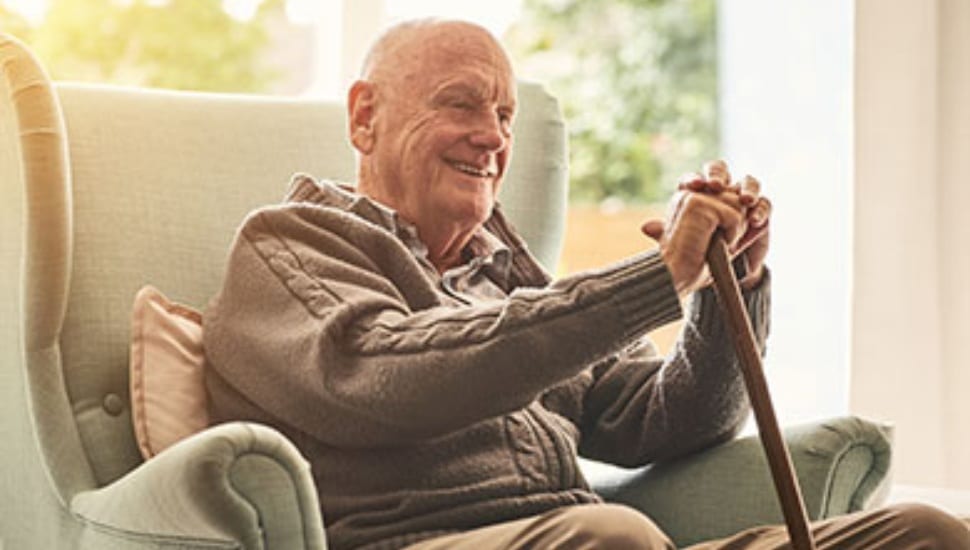 A smiling older gentleman with a cane sitting in a chair