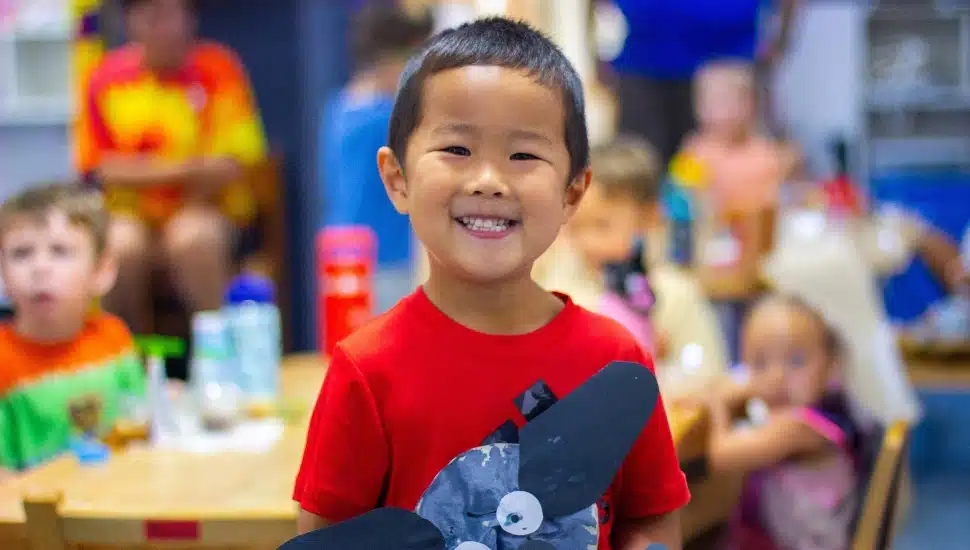 A student in an early learning classroom proudly showcases an art project.