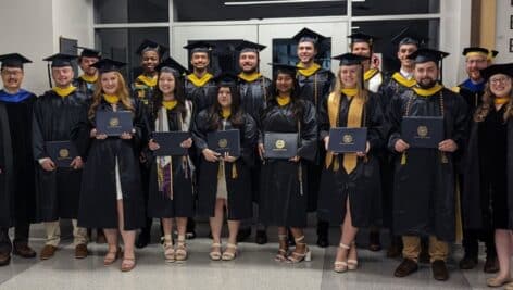 a group of students in cap and gown at wcu holding diplomas.