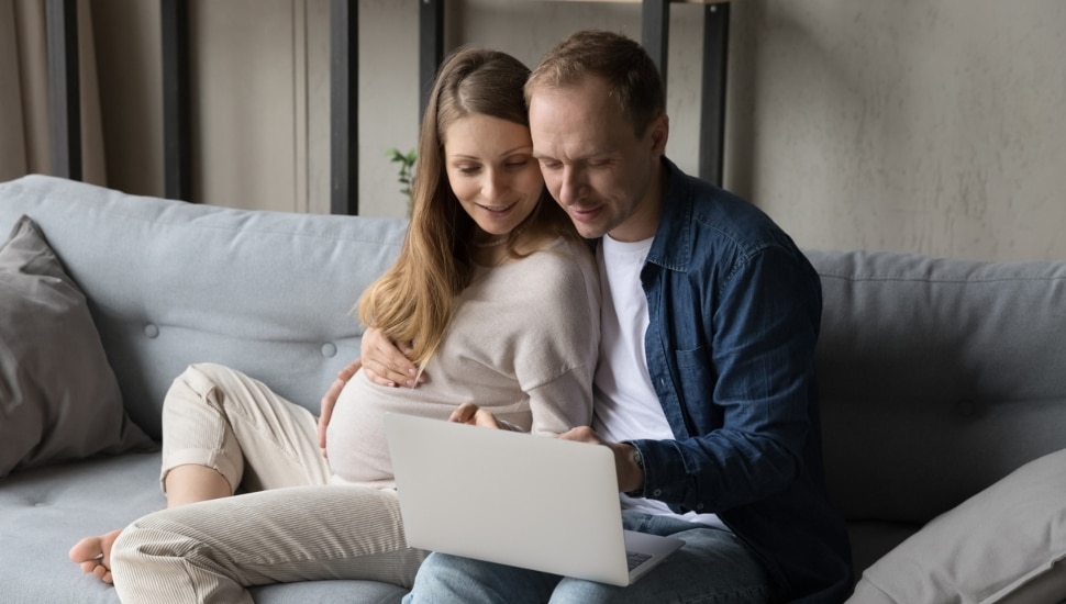 A young expecting couple attending a virtual workshop on laptop.