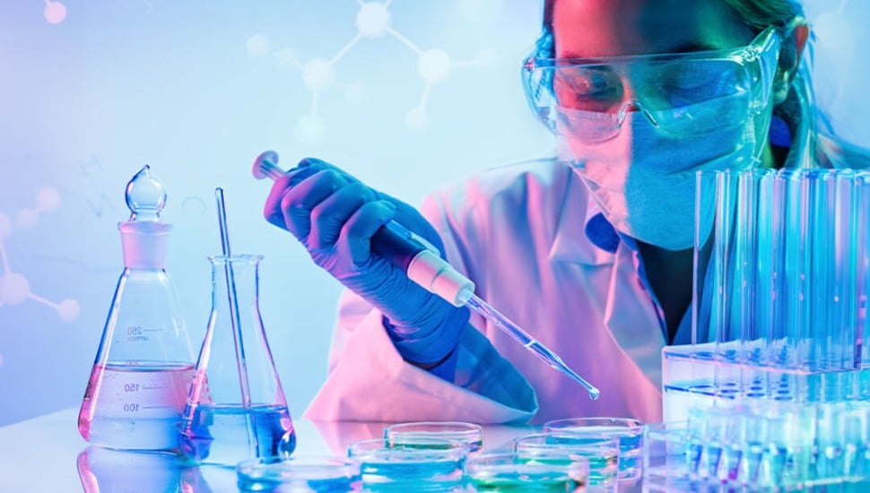 A focused student in a lab coat conducts an experiment at a laboratory bench, surrounded by glass beakers and scientific equipment.