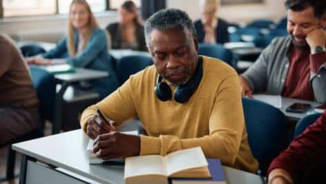 African American senior man taking notes while studying during adult educational training class in lecture hall.