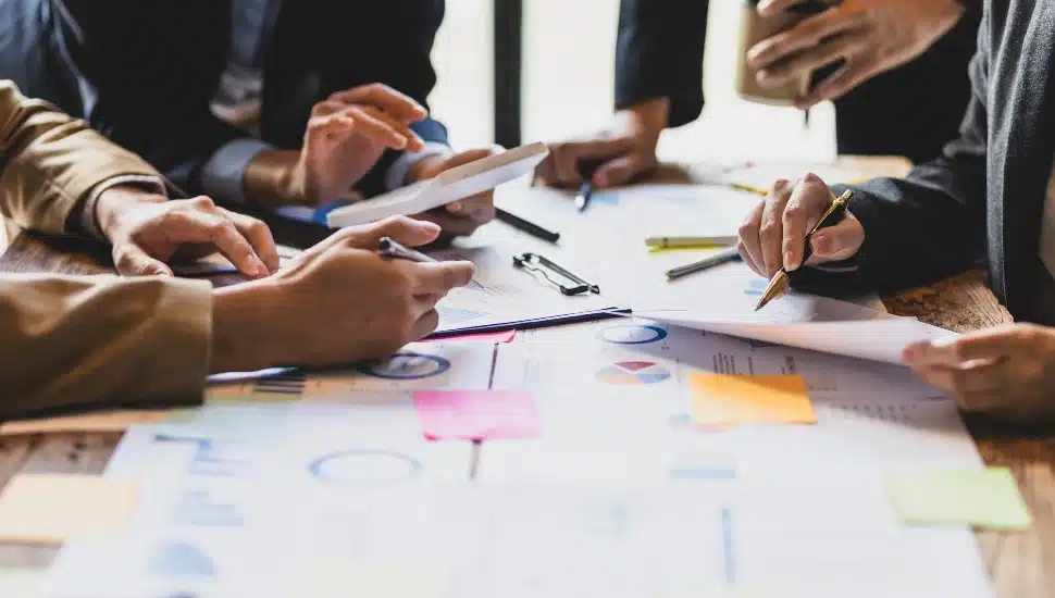 Brainstorm business meeting to discuss analysis of financial figures, graphs and growth charts of business investments to plan new business projects. Close up of charts and papers and hands gathered around a table.