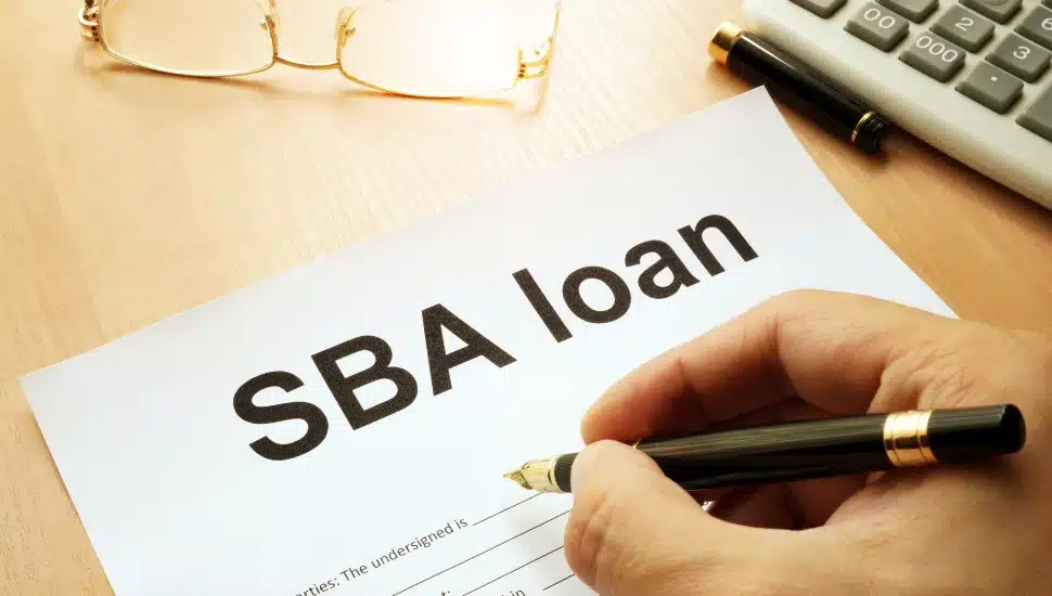A close up of a hand and paperwork for an SBA loan.