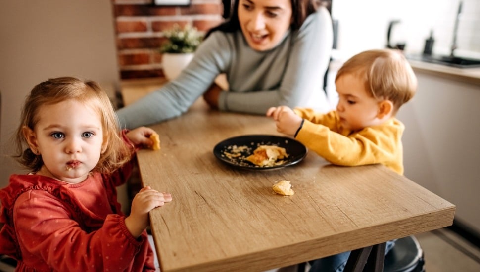 A family, with young children, eating at table.