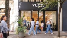 People walking along sidewalk to shop.