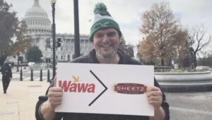 John Fetterman holding a Wawa > Sheetz sign.