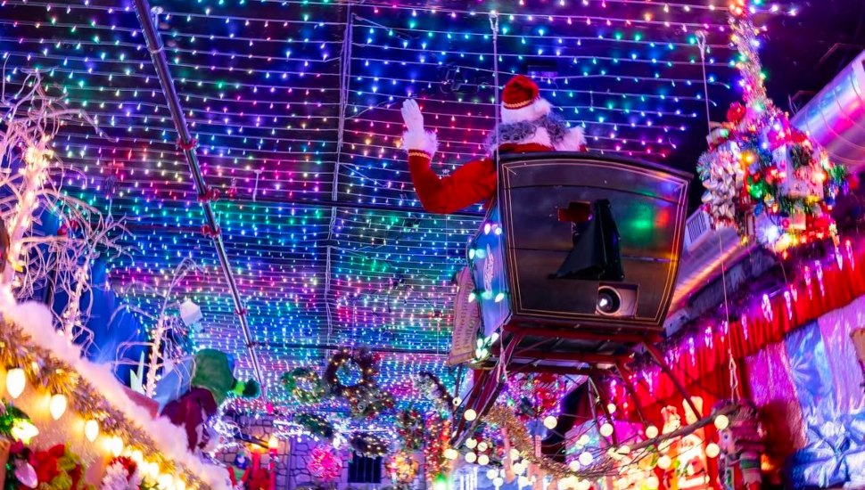 Santa mannequin on a sleigh surrounded by holiday lights on ceiling.