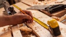 A carpenter man's hand measures with a pencil on wood.