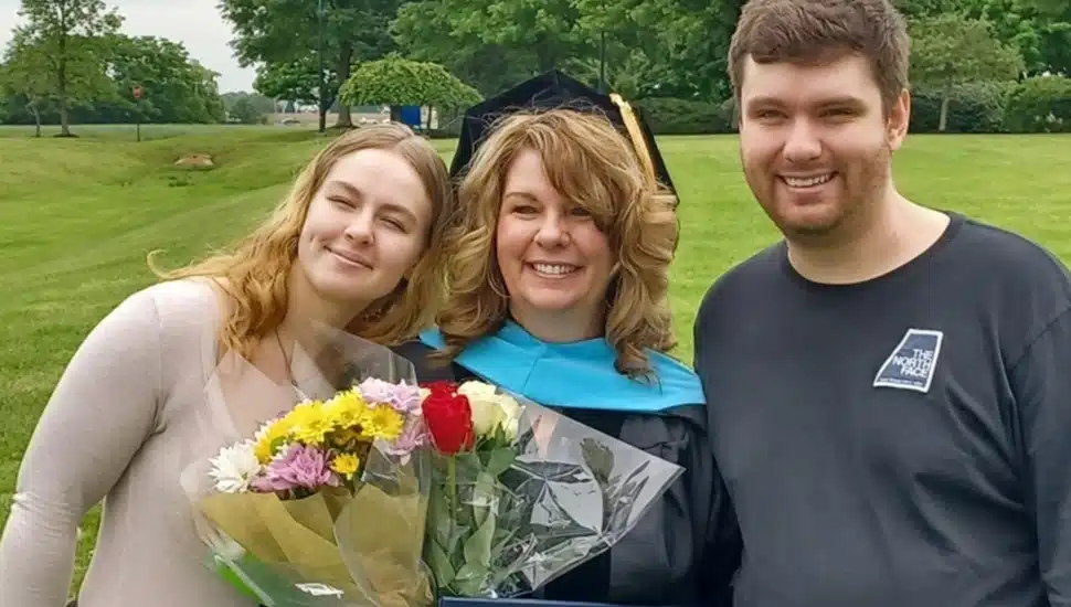College graduate in cap and gown poses for a picture with her kids.