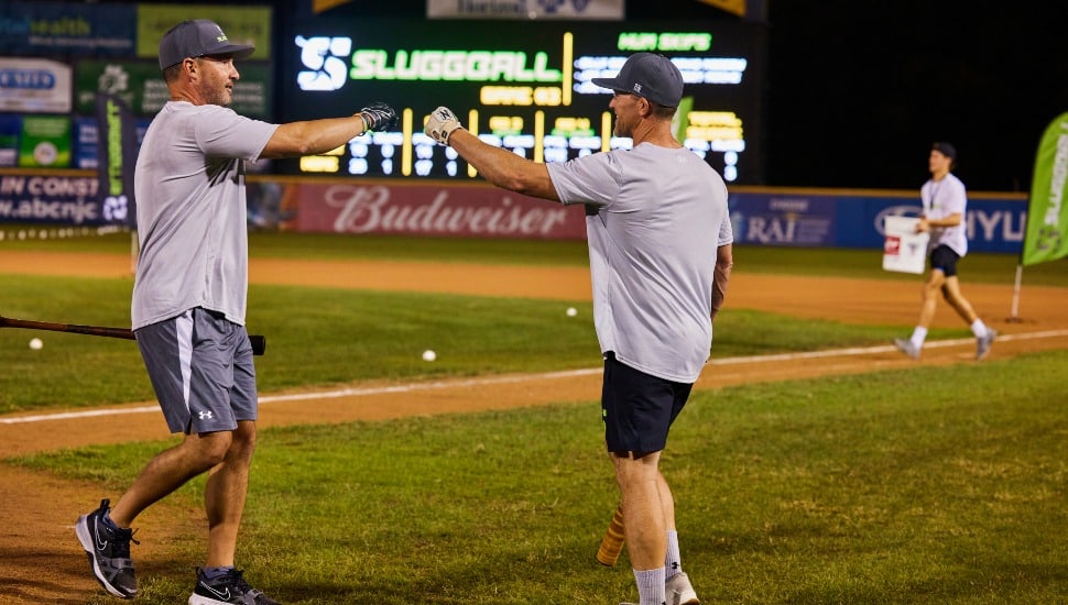 Former baseball players bump fists on a minor league field.