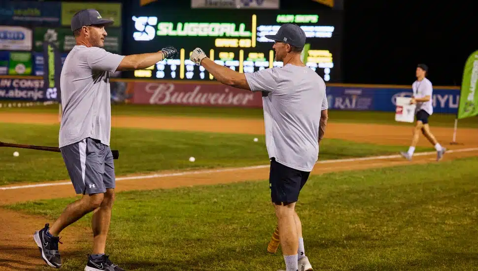 Former baseball players bump fists on a minor league field.