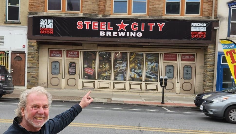 Man is pointing at a sign of Steel City Brewing.