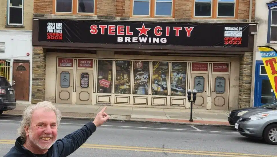Man is pointing at a sign of Steel City Brewing.