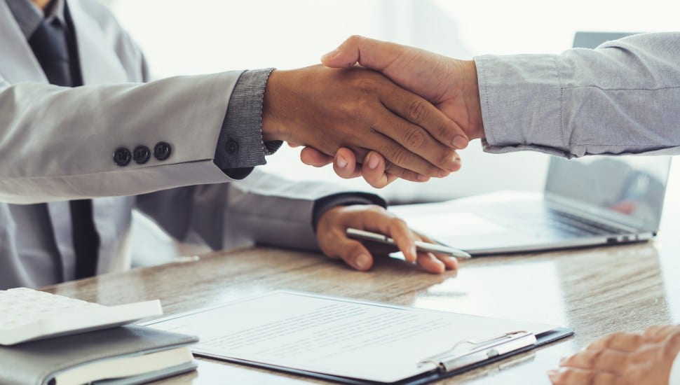 Two people shaking hands with resume in background.