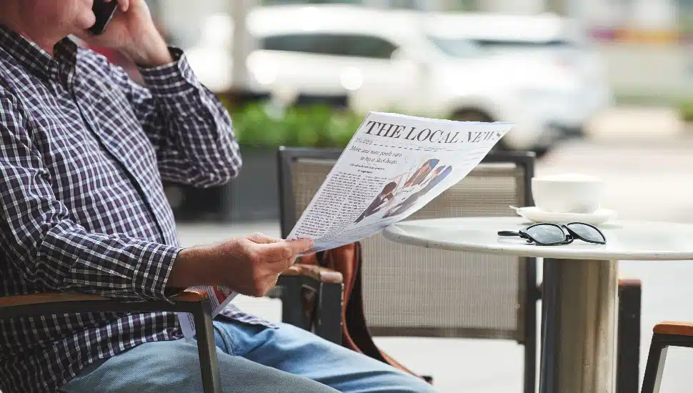 Person on the phone at a coffee shop holding a local newspaper.