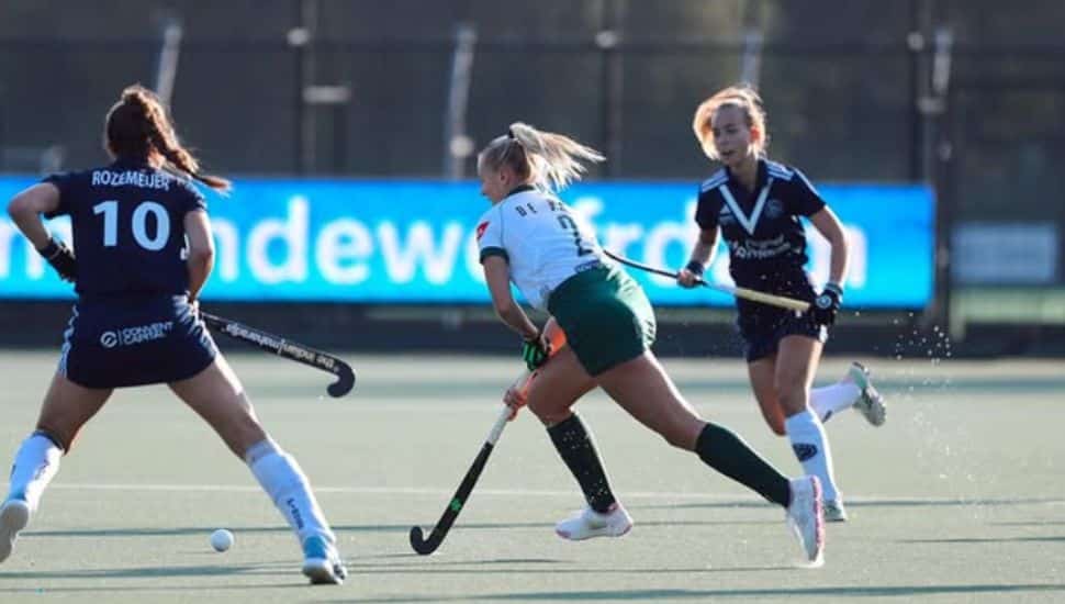 Charlotte De Vries on field hockey field playing against two opponents.