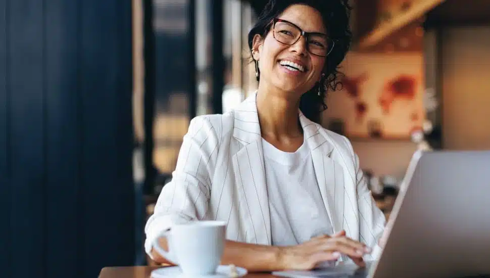Happy businesswoman working remotely on laptop in a cozy cafe.