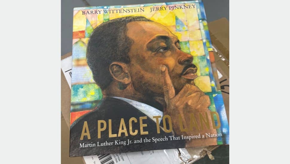 Illustrated book cover of :A Place to Land: Martin Luther King Jr. and the Speech That Inspired a Nation" by Barry Wittenstein and Jerry Pinkney, featuring a portrait of Dr. King in deep thought against a colorful stained-glass background.