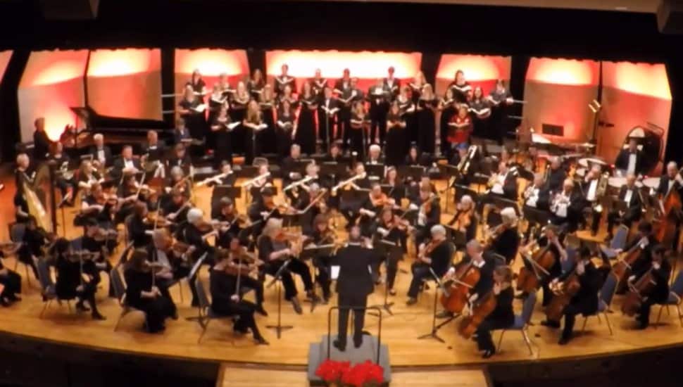 The Immaculata Symphony from above; the symphony is on stage playing in an auditorium, with composer in front.