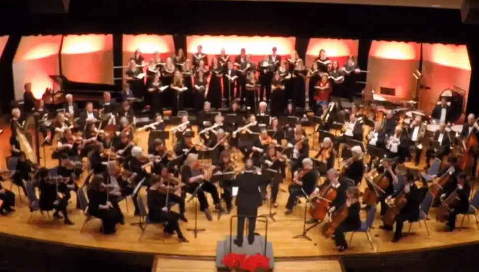 The Immaculata Symphony from above; the symphony is on stage playing in an auditorium, with composer in front.
