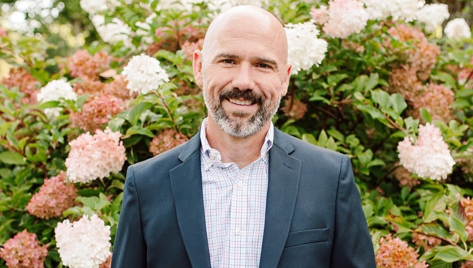Jeffrey Dolan headshot in front of flowers.