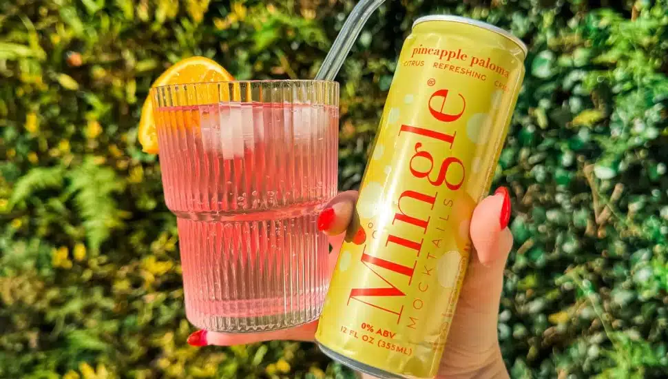 Woman's hand holding a Mingle Mocktails can and a glass.