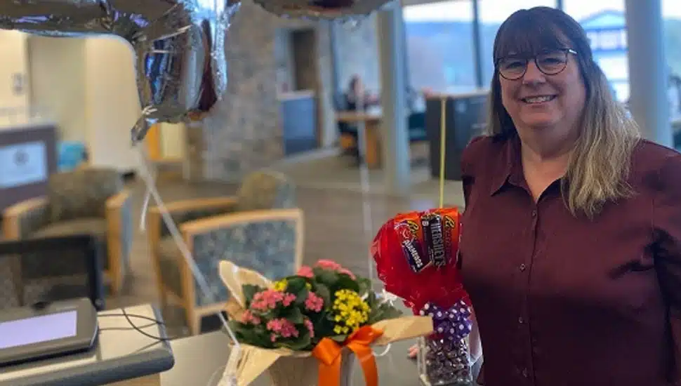 Woman celebrates 45 years working at credit union with flowers and balloons.