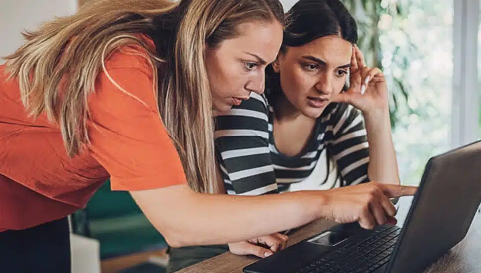 Two women look at laptop computer screen.
