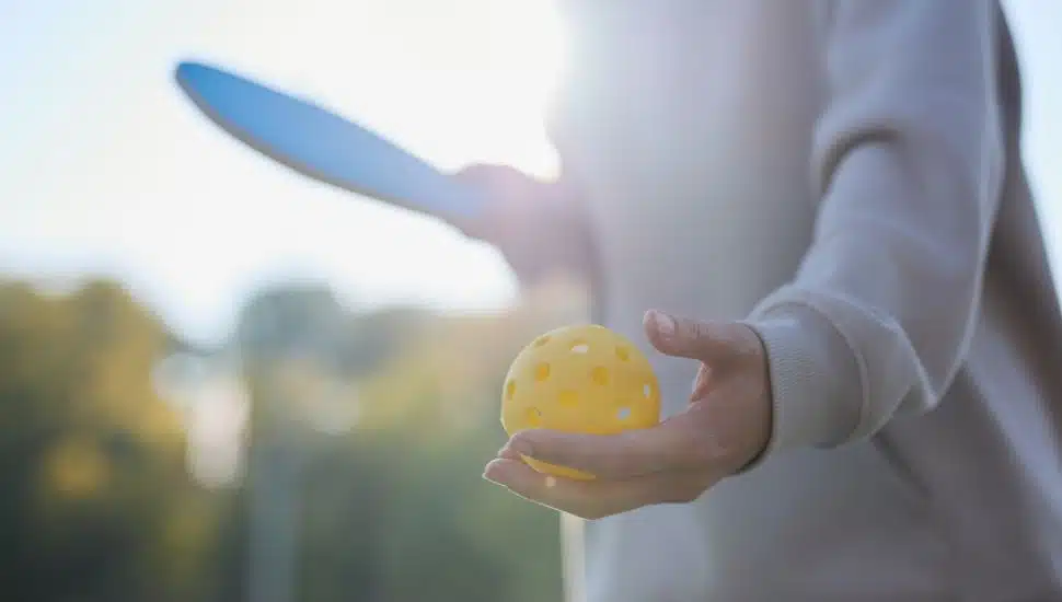 Pickleball athlete serving a ball with a racket.