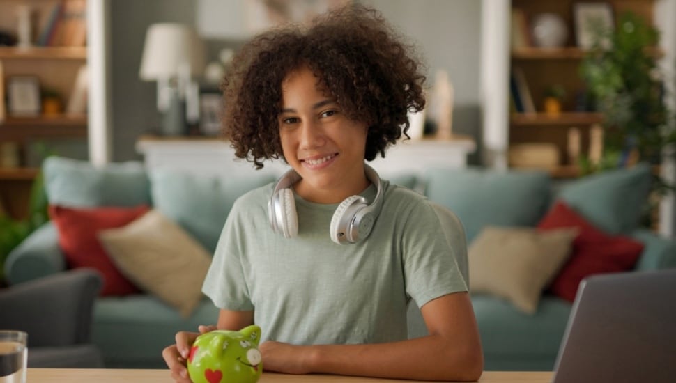 A teenager with headphones holds a piggy bank.