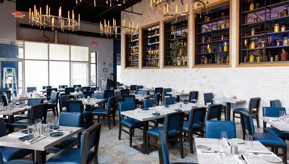 Avola Kitchen & Bar dining room with dark blue chairs and white tables.