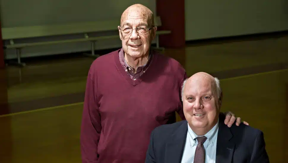 Father and son pose for a picture in a basketball gym.