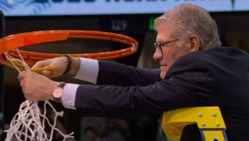 Geno Auriemma cutting a basketball net.