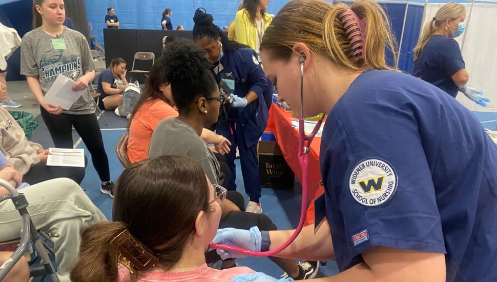 : A student nurse in a uniform checks the vital signs of a student posing as a “flood victim” in Widener University's simulated disaster drill.
