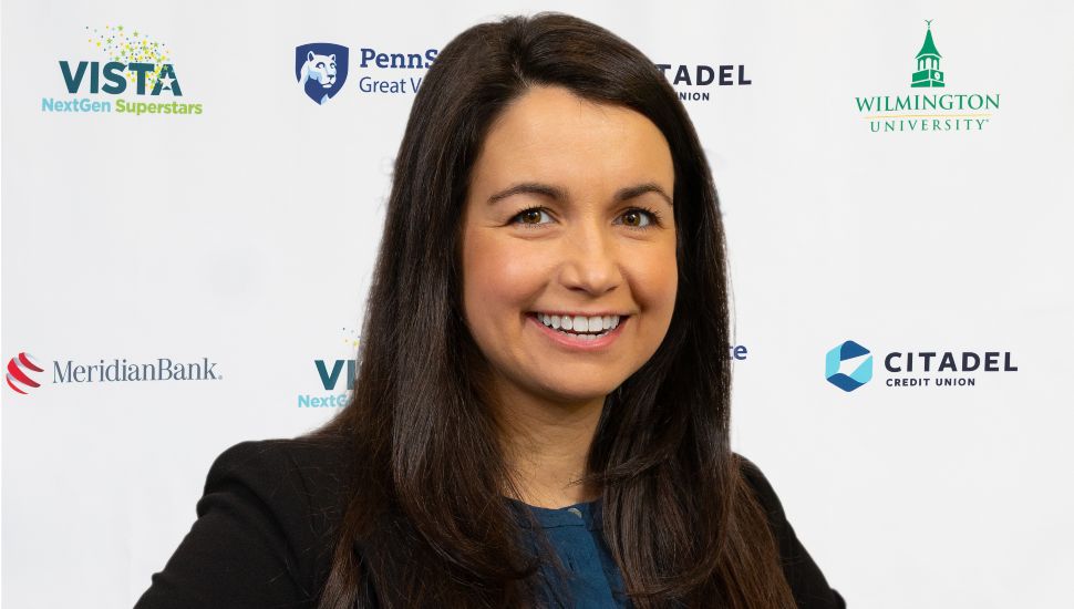 Headshot of Katelyn Lloyd. She is smiling, in front of a sponsor banner, and has long dark hair and a dark blazer on.