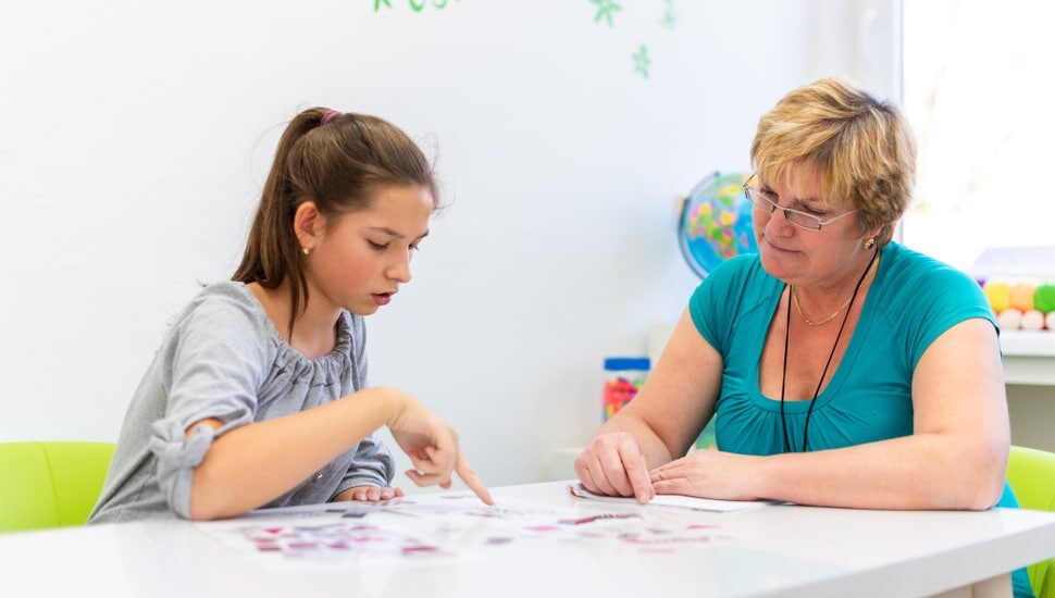 A woman therapist sitting at a table with a teenage girl as they work on a project together.