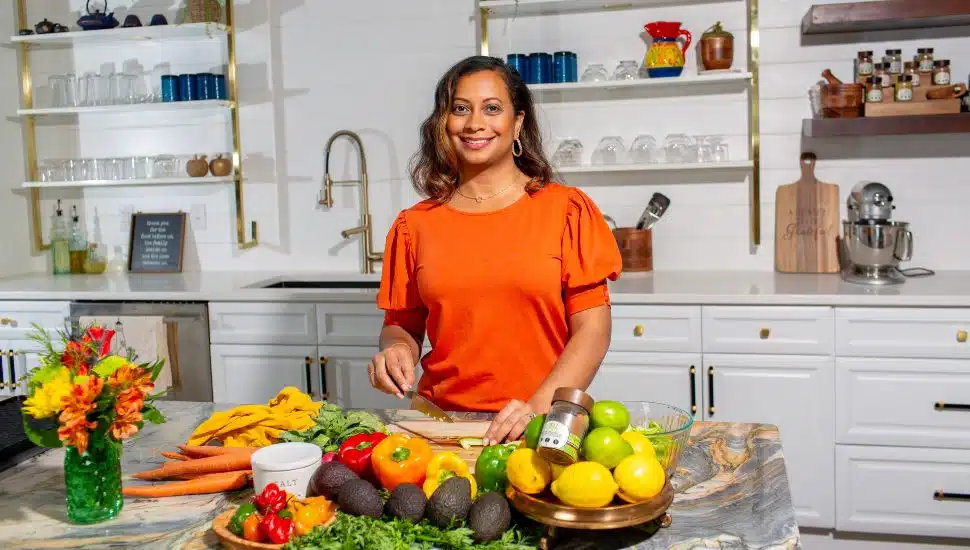 Tashelle Darby-Wong in an orange shirt cutting fruits and veggies at kitchen counter.