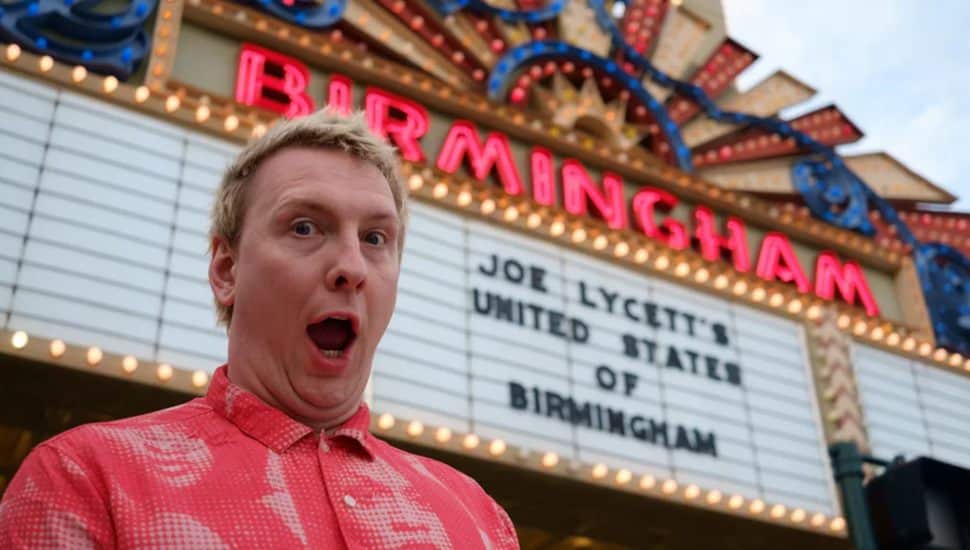 Joe Lycett standing in front of a movie theater outside with the movie sign saying 'United States of Birmingham.'