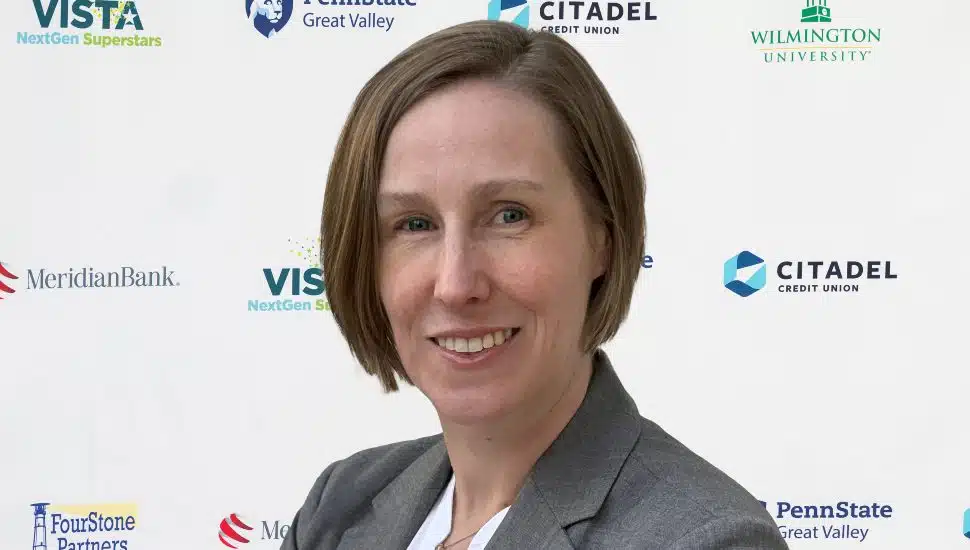 Headshot of Elise Corbin positioned in front of the VNS NextGen Superstars banner. She is smiling and has short brown hair and wears a gray blazer and white shirt.