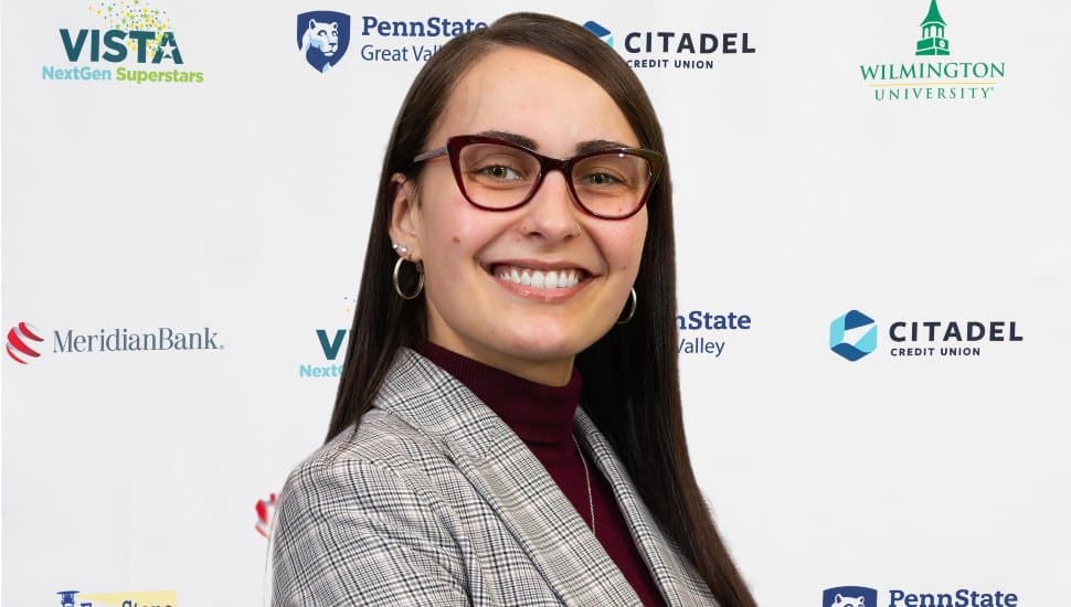 Headshot of Jessica Finley wearing glasses and plaid blazer. Finley is turned to the side and looking over shoulder smiling. She has dark brown long hair and glasses.