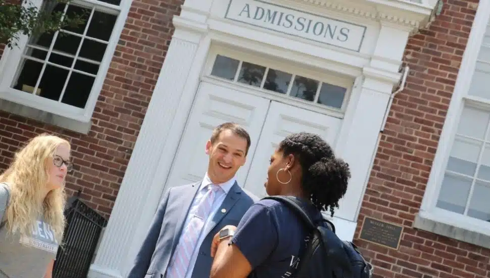 Joe Howard talking to students on campus with the Admissions Building in the background.