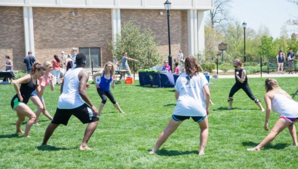 Students gathered in a circle on the lawn at WCU on a sunny day stretching/moving.