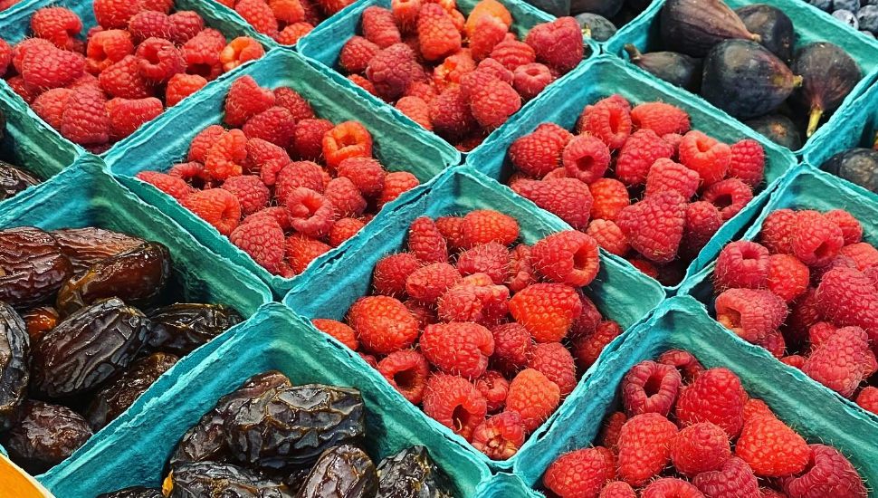 Raspberries and other fruits in green cartons for sale at farmers markets.