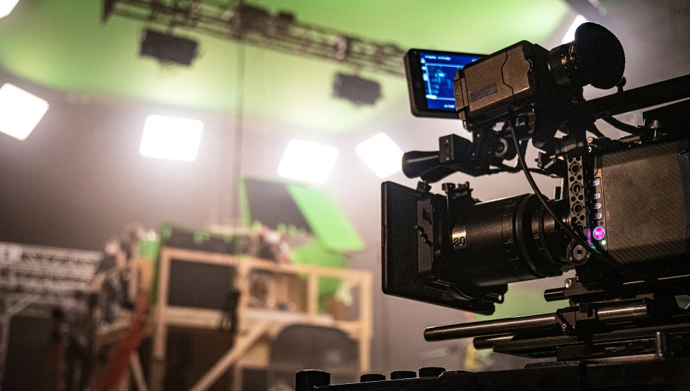Film studio set up with camera and green screens.