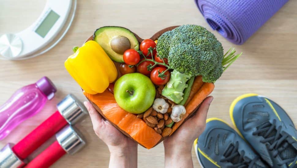 Healthy lifestyle, heart dish filled with food. Exercise equipment on sides of heart dish.