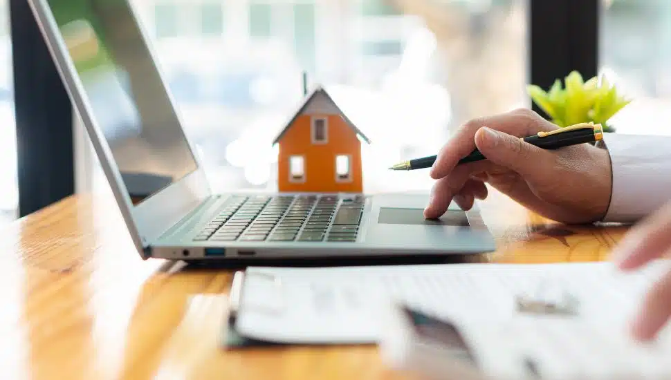 Housing concept of person on laptop with little house next to it.
