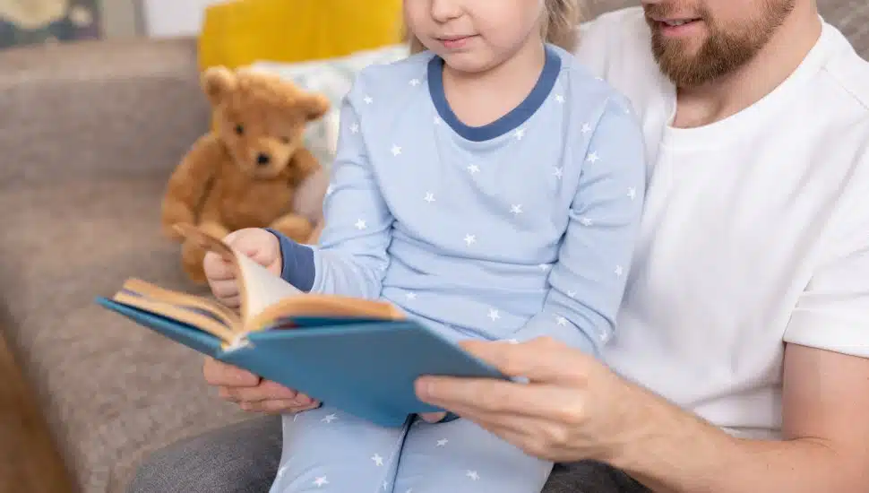 Family of young father and his little daughter in blue pajamas reading together.