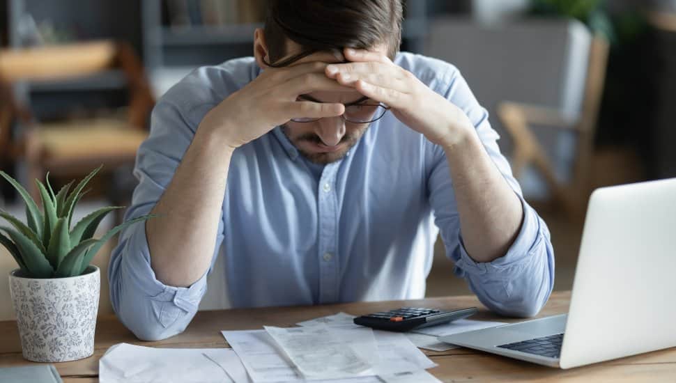 Stressed man holding head in hands looking at tax documents and payments.