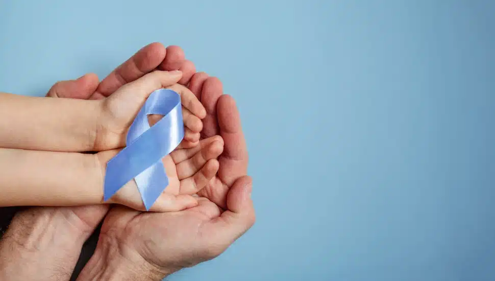 A child holds a blue ribbon symbolizing National Child Abuse Prevention Month, cradled in her father's hands.